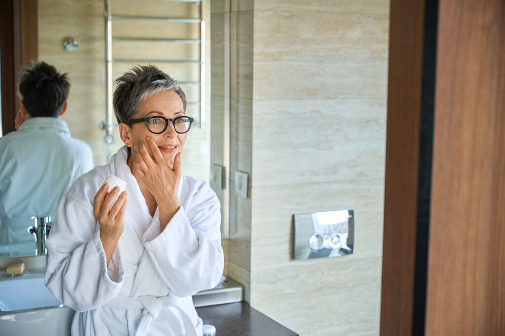 Woman applying face cream in a bathroom mirror
