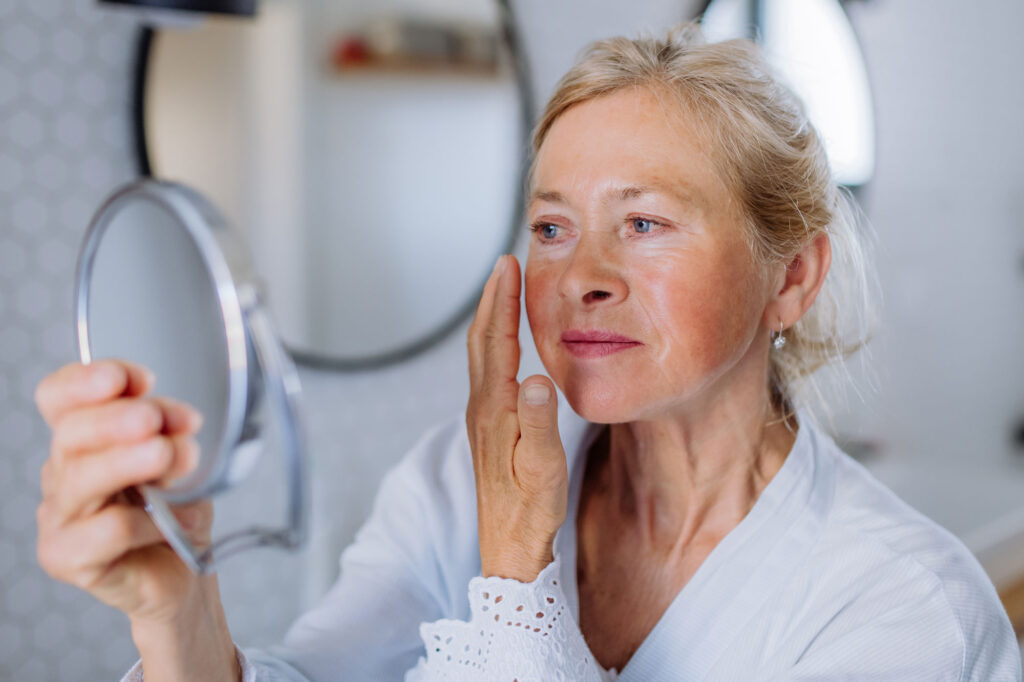 Older woman examines facial skin with handheld mirror