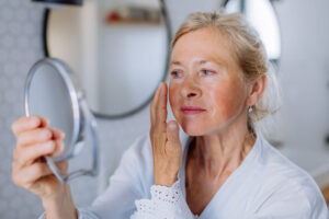 Older woman examines facial skin with handheld mirror