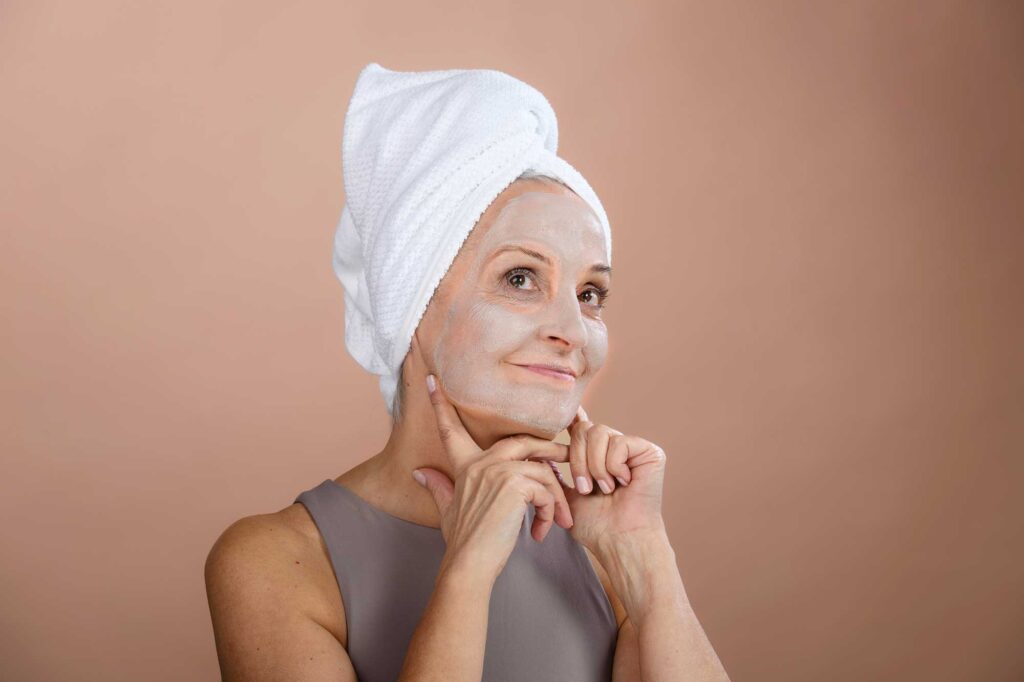 Woman with towel turban applies facial skincare mask