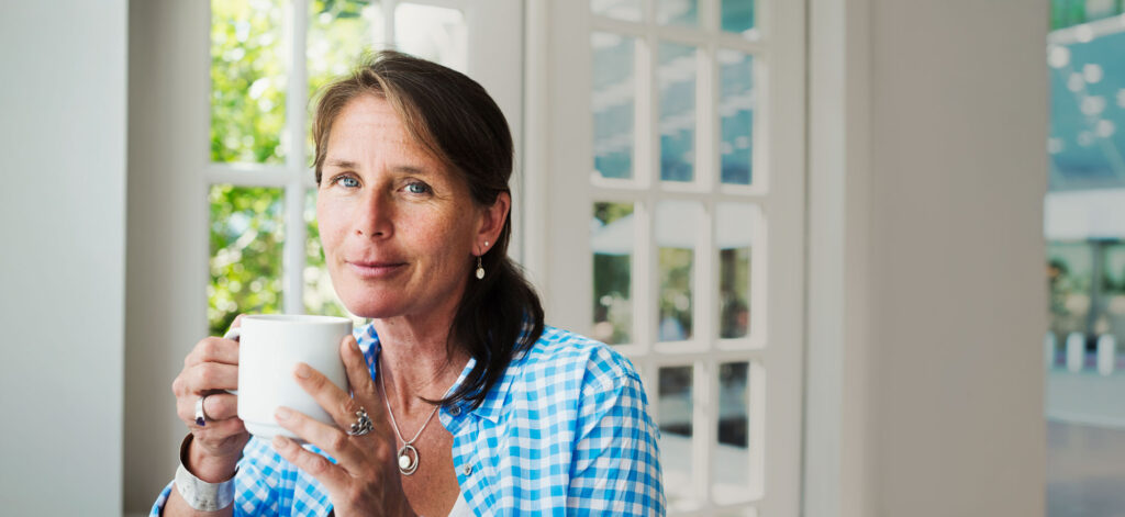 Woman holding a white mug near a bright window