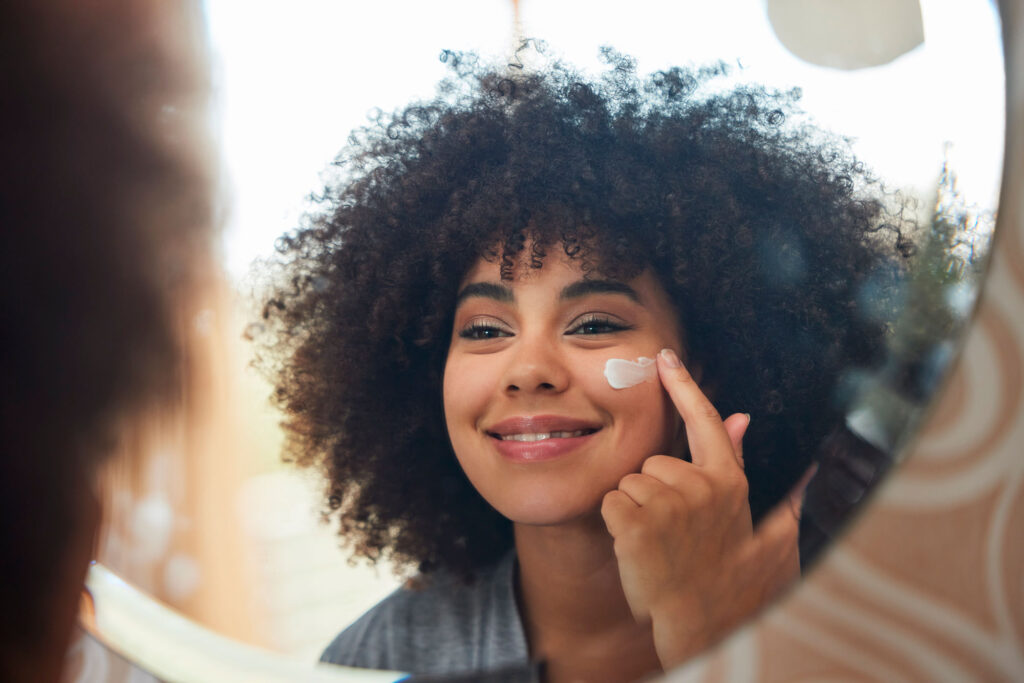 Woman applies face cream while looking in mirror