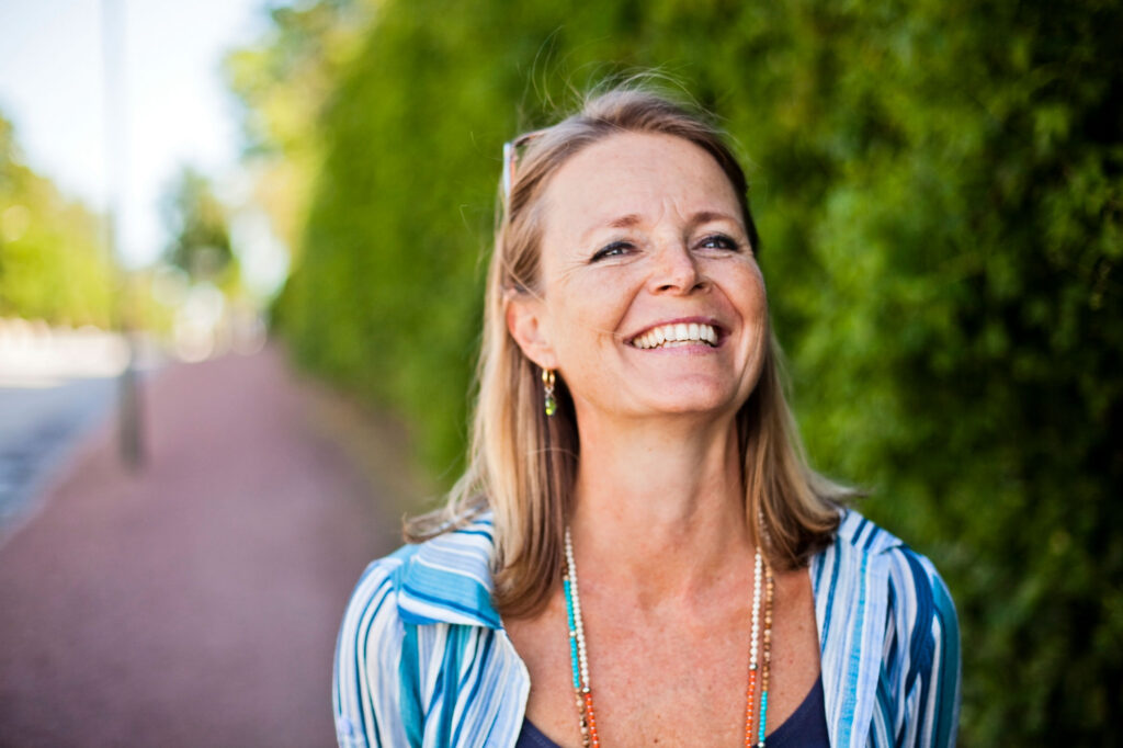 Smiling woman outdoors beside lush green foliage