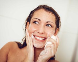 Smiling woman washing her face with foamy cleanser