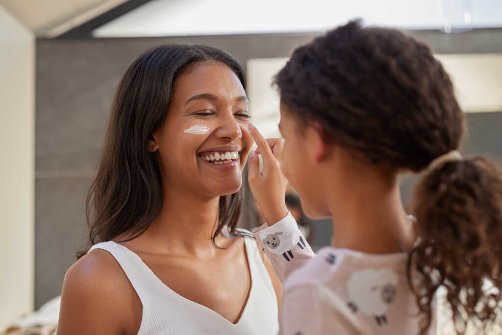 Child applies face cream to smiling mother's cheek